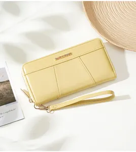Detailed view of yellow women long zip wallet with wrist strap and metal logo accent.