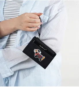 Detailed shot of a black short wallet with cute puppy embroidery, zipper and wrist strap.