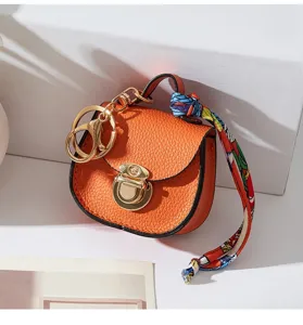 Mini borsa a sella portachiavi arancione con chiusura in metallo dorato e foulard colorato.