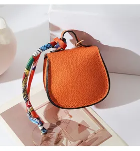 Dettaglio mini borsa a sella in pelle con finitura arancione testurizzata e nastro.