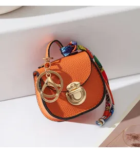 Mini borsa portachiavi in pelle arancione con dettagli dorati e foulard decorativo elegante.