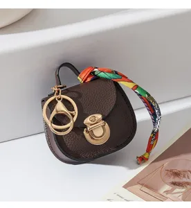 Mini borsa a sella in portachiavi in pelle con accessori metallici e foulard twilly colorato.