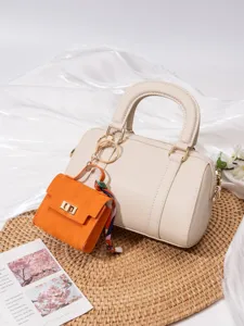 Schicke beige Zylindertasche mit leuchtend orangefarbenem Minitaschen-Anhänger und edlem Seidentuch.