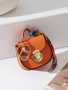 Portachiavi mini borsa a sella in pelle arancione con dettagli dorati e foulard colorato.
