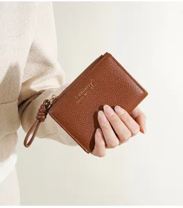 Gros plan détaillé du portefeuille en cuir marron avec texture grainée, fermeture éclair et lanière.
