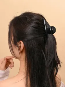 Close-up detail shot of a woman wearing a black plastic hair claw clip for styling hair.