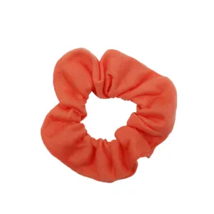 Primo piano dettaglio di scrunchie in tessuto arancione corallo, materiale cotone morbido, accessorio.