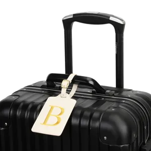 Étiquette de bagage en cuir beige avec lettre brodée dorée B, porte-nom de voyage élégant.