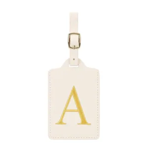 Étiquette de bagage en cuir crème avec lettre brodée dorée et boucle en métal pour voyage.