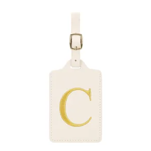 Étiquette de bagage en cuir beige avec lettre C brodée dorée et sangle à boucle.