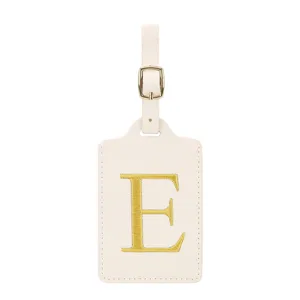Etiquette de bagage en cuir beige avec broderie lettre E dorée et boucle métal pour voyage.