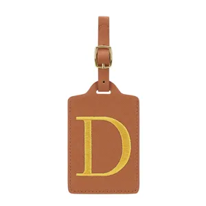 Détail étiquette de bagage en cuir PU marron, lettre D brodée dorée, accessoire de voyage durable.