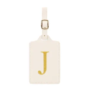 Étiquette de bagage en cuir beige avec lettre J brodée dorée et une boucle en métal.