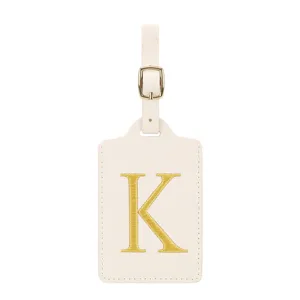 Détail d'étiquette de bagage en cuir beige avec monogramme brodé doré et boucle.