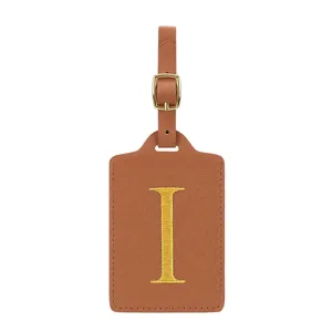 Gros plan sur l'étiquette de bagage en cuir PU marron avec boucle dorée et lettre jaune.