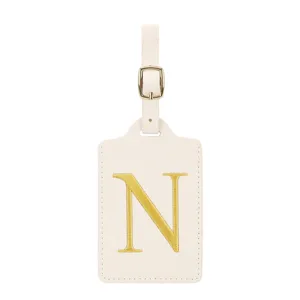 Détail étiquette de bagage lettre N brodée or, cuir PU beige avec boucle de réglage.