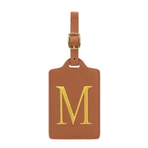 Gros plan détail d'étiquette de bagage en cuir PU marron avec lettre M brodée dorée et boucle.