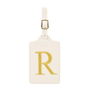Gros plan détaillé de l'étiquette de bagage beige avec lettre R brodée et boucle dorée.