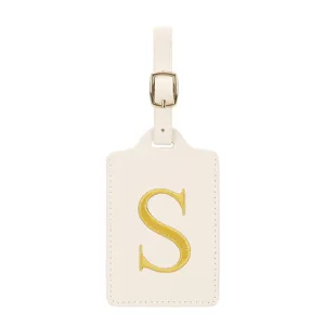 Vue détaillée de l'étiquette de bagage beige avec lettre brodée dorée S et boucle métallique.