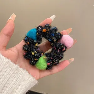 Close-up of fluffy winter wool hair scrunchie with colorful pom pom details on hand model.