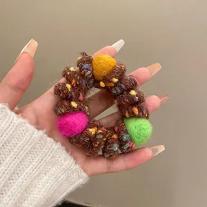 Detailed shot of a fluffy wool telephone wire hair scrunchie with colorful pom pom balls.