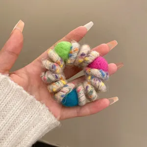 Detailed close up view of colorful wool wrapped telephone cord hair tie with cute pom poms.