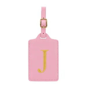 Dettaglio etichetta bagaglio in ecopelle rosa con lettera J ricamata oro e fibbia.