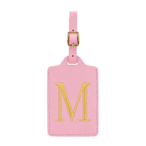 Dettaglio dell'etichetta bagaglio in ecopelle rosa con lettera M ricamata in oro e fibbia.