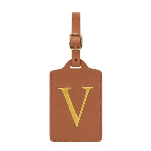 Gros plan détaillé d'une étiquette de bagage en cuir PU marron avec lettre V brodée en or.