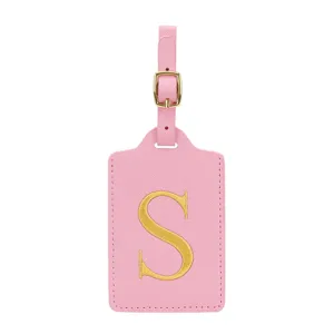 Dettaglio etichetta bagaglio in pelle PU rosa con lettera ricamata oro e fibbia metallica lucida.