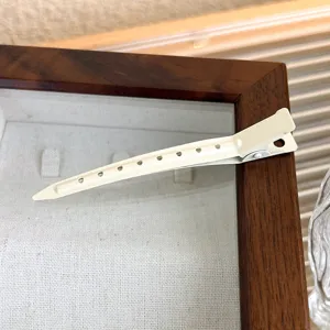 Close-up view of a beige duckbill hair clip placed on a wooden display tray, highlighting fine details.