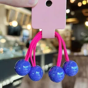 Close-up detail of candy-colored elastic hair ties with glossy blue ball charms on card.