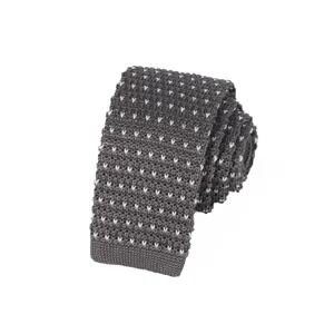 Close-up detail of dark grey knitted tie with white dot pattern, showing fine texture.