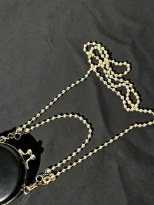 Close-up detail van de mini zwarte PU ronde tas met elegante gouden bal ketting riem stijl.