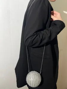 Detail shot of a stunning rhinestone spherical evening bag with chain strap worn on black blazer.