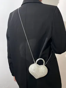 Vista dettagliata della borsa a tracolla lucida con strass a cuore e catena metallica.