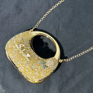 Nahaufnahme der luxuriösen, goldfarbenen Kristall-Handtasche mit Kette und Logo-Detail.