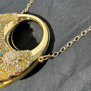 Detailaufnahme einer glänzenden Strass-Abendtasche mit Goldkette und Metallringgriff.