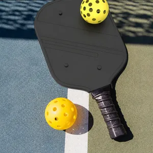 Pickleball-set met duurzaam zwart racket en twee gele geperforeerde ballen voor buiten op de baan.