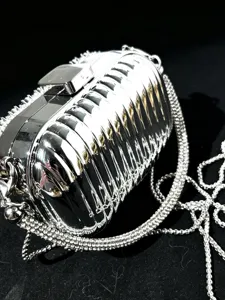 Silbrige metallische Rippen-Clutch-Detail mit Strass-Kettenriemen und glänzender Textur.