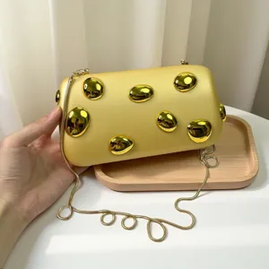 Detailaufnahme der trendigen Acryl-Umhängetasche in Gelb mit Metallnieten und goldener Kette.