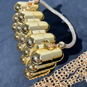 Gold capsule evening clutch bag detail showing shiny metallic pill shape and chain strap.