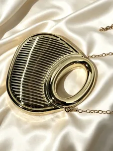 Nahaufnahme der metallisch goldenen Abendtasche mit Rillenstruktur und rundem Griffdetail.