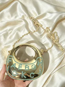 Nahaufnahme der goldenen metallischen Crescent-Umhängetasche mit Glitzerbuchstaben und Kette.
