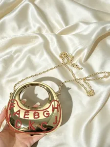 Detailaufnahme der goldenen Mondsichel-Umhängetasche mit roten Glitzerbuchstaben und Kette.