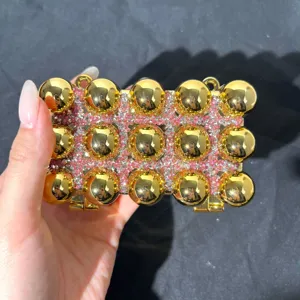 Detail of acrylic evening clutch bag with gold balls and pink rhinestones for women.