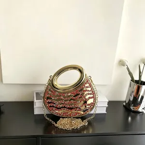 Detailaufnahme der goldenen Acryl Abendtasche mit roten Strasssteinen und Metallring.