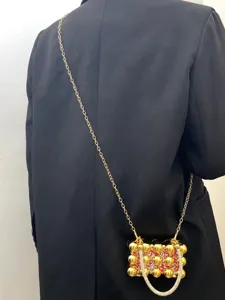 Detail view of stylish acrylic evening bag with gold spheres, red rhinestones and metal chain.