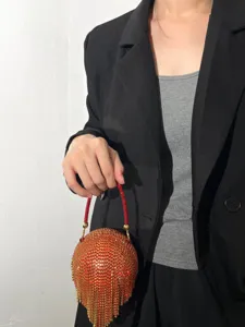 Gros plan d'un sac de soirée rond étincelant en strass avec poignée perlée rouge et franges.