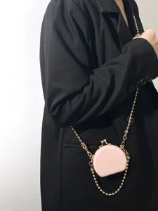 Detailgezicht van een roze mini hardcase lippenstiftas met gouden ketting gedragen op zwarte blazer.